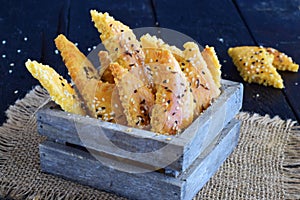 Salty biscuits with sesame seeds in a wooden box on an abstract grey background.