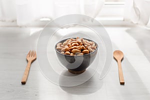 Salty cashew nuts in black ceramic bowl on wood