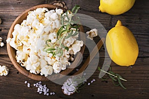 Salty crunchy fresh homemade popcorn flavored with lemon peel and rosemary scent in a wooden bowl on simple background