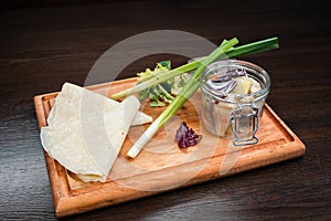 Salty herring, fresh green onions, red onions, greens and pita on a wooden board in a restaurant. Delicious marinades and pickles.