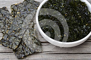 Salty roasted dried seaweed nori with sesame seeds in a blue bowl on old wooden table. Healthy snack,Korean food concept.