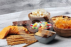 Salty snacks. Pretzels, chips, crackers in wooden bowls and candy and chocolate on table