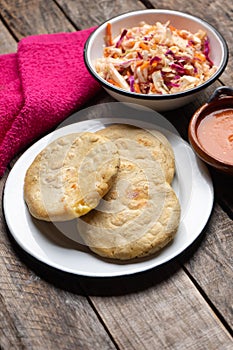 Salvadoran pupusas with coleslaw and tomato sauce on wooden background