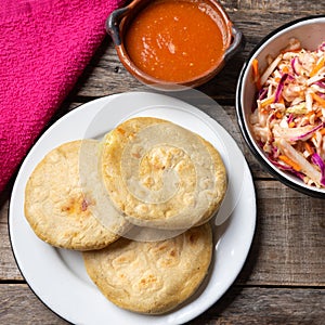 Salvadoran pupusas with coleslaw and tomato sauce on wooden background