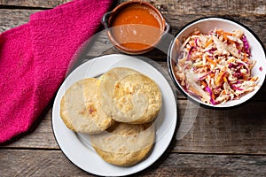 Salvadoran pupusas with coleslaw and tomato sauce on wooden background