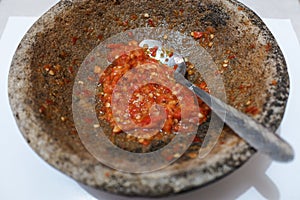Sambal or traditional chili sauce from Indonesia, freshly made using stone mortar and spoon, Isolated in white background