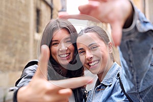 Same Sex Female Couple Pose For Photo Making Shape Of Frame With Hands As They Visit City Together