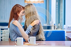 Same-sex relationships. Happy lesbian couple sitting in a cafe. Girls gently hold hands and drink coffee. Embrace of