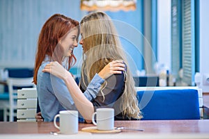 Same-sex relationships. Happy lesbian couple sitting in a cafe. Girls gently hold hands and drink coffee. Embrace of