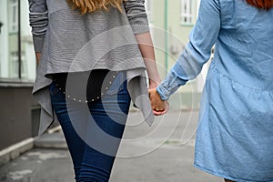 Same-sex relationships. Happy lesbian couple walking down the street holding hands. The backs of two beautiful women on