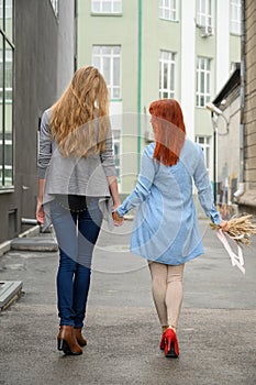 Same-sex relationships. Happy lesbian couple walking down the street holding hands. The backs of two beautiful women on