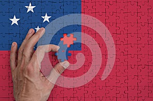 Samoa flag is depicted on a puzzle, which the man`s hand completes to fold