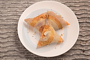 Samosas a spicy blend of vegetables or meat wrapped in a deep fried triangular pastry parcel in a white plate.