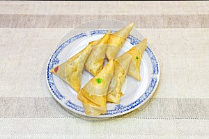 samosas stuffed with meat and vegetables marked to distinguish them on a blue rimmed plate and on a beige table in a Pakistani