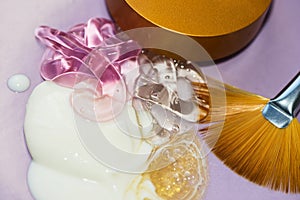 Samples of cosmetic creams with golden fan brush and cap on violet background