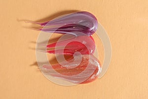 Samples of different lipglosses on beige background, top view