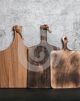 Samples of three different rustic wooden cutting boards on a kitchen countertop against a concrete wall. Manufacture of
