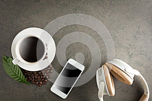 Samrtphone with headphone and cup of coffee on stone background.
