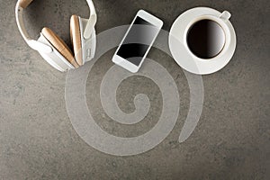 Samrtphone with headphone and cup of coffee on stone background.