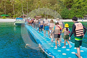 SAMUI ISLAND, THAILAND - OCTOBER 13, 2019 : Group of tourists walking on plastic pontoon walk way floating in the sea go to the