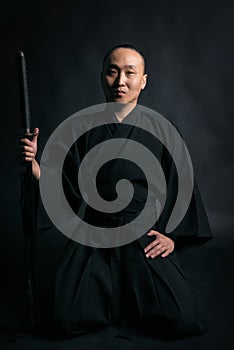 Samurai in black kimano with sword in hands on a black background