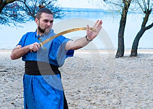 Samurai in blue kimono, bun and sticks on head training with sword and looking away