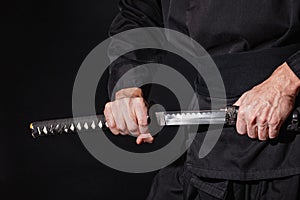 The samurai holding a Japanese katana sword. Photo of a warrior dressed in black clothes in low key with selective