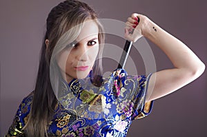 Samurai woman dressed in traditional colorful flower pattern asian silk dress, holding arm over shoulder grabbing sword