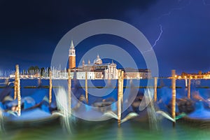 San Giorgio Maggiore church and gondolas in Venice, Italy during blue hour with dramatic sky and lighting. Focus on the church.