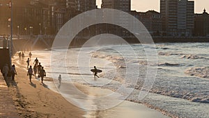 San Lorenzo, Gijon beach and waterfront, at sunset. Unkown people on the sand; a surfer coming out of the sea with his board. Astu