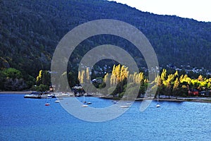 San Martin de los Andes, lake and transparent waters with wooden pier and tourist boats, white sand beaches with poplar tree in