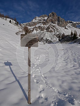 San Pellegrino valley pass hiking Tour wooden sign and rocky Dolomites mountain covered in snow