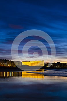 Kursaal auditorium illuminated at night is reflected in the beach of Zurriola, city of San Sebastian