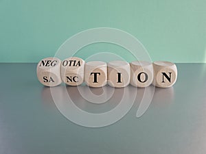 Sanction or negotiation symbol. Turned cubes and changes the word sanction to negotiation. Beautiful grey table, blue background.