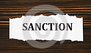 SANCTION - word on a white tattered piece of paper on a wooden background