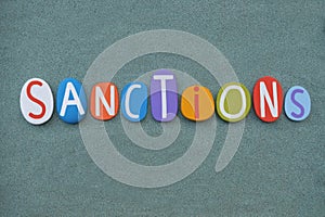 Sanctions, creative word composed with multi colored stone letters over green sand photo