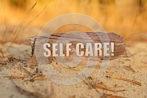 On the sand against a background of yellow grass, a signboard with the inscription - SELF CARE