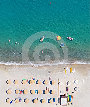 Sand beach aerial view, vertical shot. Sunbeds, sunshades and water sports equipment, people swimming and taking sunbath