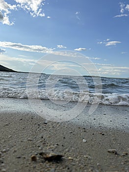Sand beach and blue sea. Close up soft wave lapped the sandy beach. Beautiful sea waves with foam of blue and turquoise