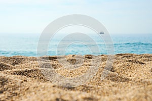 Sand on the beach close up with blurred sea, ship and waves on a background.