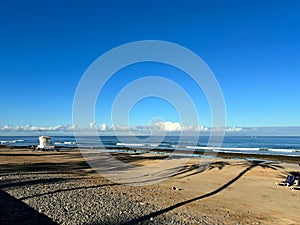 Sand beach on the coast of Las Americas, yellow sand, palm trees shadows, blue sky and waves, Tenerife, Canary Islands, Spain