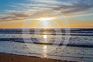 Sand beach with endless horizon and foamy waves under the bright sundown with yellow colors and clouds above the sea