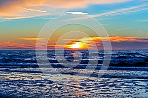 Sand beach with endless horizon and foamy waves under the bright sundown with yellow colors and clouds above the sea