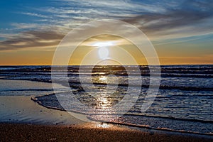 Sand beach with endless horizon and foamy waves under the bright sundown with yellow colors and clouds above the sea