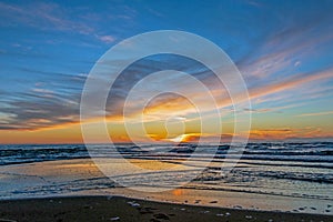 Sand beach with endless horizon and foamy waves under the bright sundown with yellow colors and clouds above the sea