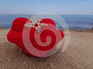 on the sand on the beach, a toy red soft heart hugs a snowflake with its hands. Christmas on the beach.