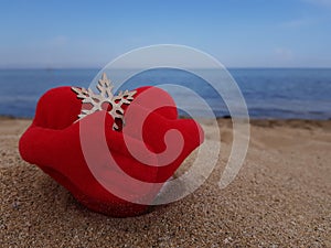 on the sand on the beach, a toy red soft heart hugs a snowflake with its hands. Christmas on the beach.