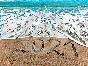 On the sand of a beautiful beach is written 2021. The concept of a Happy New year.