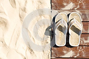 Sand and flip flops on boardwalk at sunny beach.