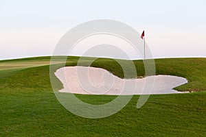 Sand bunker in front of golf green and flag